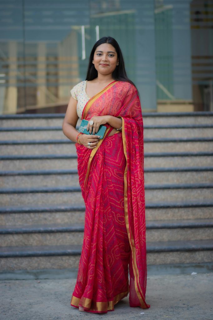 Portrait of a woman in a vibrant red saree standing on urban steps in New Delhi.